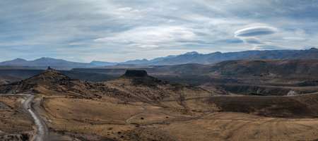 Dramatic arid landscape panoramic view with mesa formations leads to hazy distant mountains under a partly cloudy sky. North of Neuquen, Argentinaの写真素材
