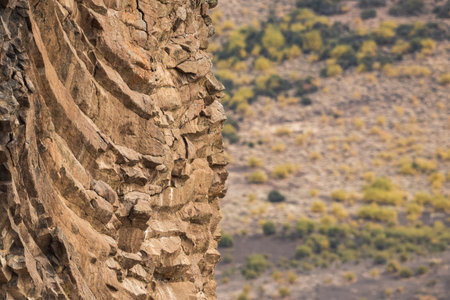 Detailed view of a rugged basalt rock face in Patagonia, with blurred vegetation in the backgroundの写真素材