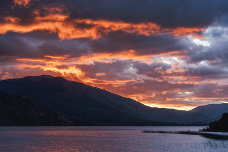Dramatic sunset sky with fiery orange and dark clouds over a tranquil lake and silhouetted mountains in Patagonia. Ãorquinco, Neuquen, Argentinaの写真素材