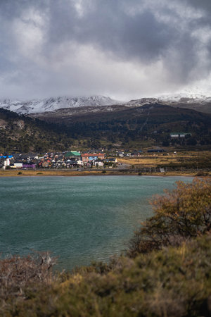 Caviahue town nestled on the shore of lake, with snowcapped mountains rising in the background under a cloudy sky. Neuquen, Argentinaの写真素材