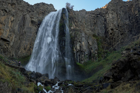 Woman looking at big waterfall with crystal clear water falling over rocks and moss. Manzano Amargo touristic destination, Neuquen, Argentinaの写真素材
