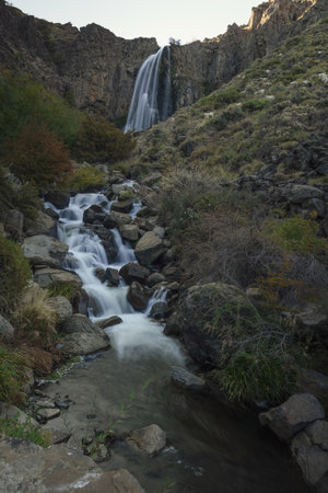 Picturesque waterfall low angle shot cascading from cliff rock formations surrounded by wild vegetation and goats eating grassの写真素材