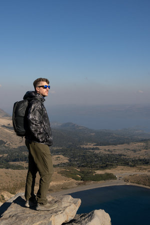 Man stands on a rocky mountain top, overlooking the Batea Mahuida Volcano and a vast landscape under a clear sky. Villa Pehuenia, Neuquen, Argentinaの写真素材