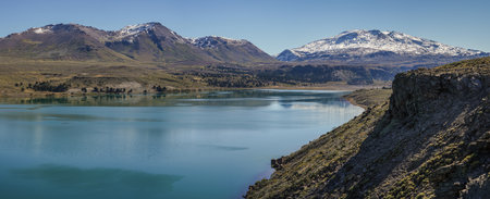 Turquoise waters of Lake Caviahue under rocky landscape and snowcapped Copahue volcano under a clear blue sky. Caviahue, Neuquen, Argentinaの写真素材