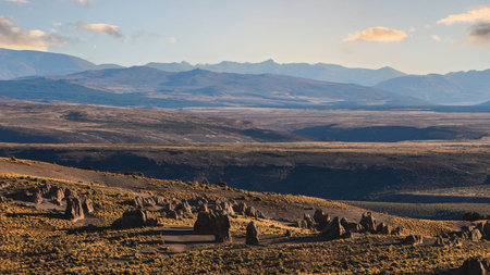 Rugged, brown terrain with unique rock formations under a clear sky. Distant mountains in arid landscape in Los Bolillos, Neuquen, Argentinaの写真素材