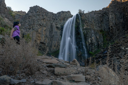 Brunette Woman Contemplates Cascada La Fragua in Rocky arid Landscape. Manzano Amargo tourist destination, Neuquen, Argentinaの写真素材