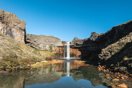 Scenic view of Salto del Agrio waterfall cascading into the Agrio River, surrounded by rocky cliffs under a clear blue sky. Neuquen, Argentinaの写真素材