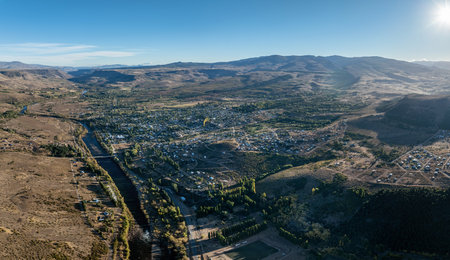 High-angle shot: town nestled in a vast Patagonian valley in Alumine with a river and surrounding mountains under a clear sky. Neuquen, Argentinaの写真素材
