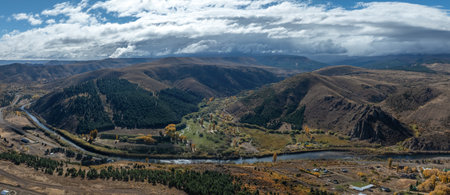 High-angle view: Alumine town nestled beside a blue river in the vast Patagonian landscape under a partly cloudy sky. Neuquen, Argentinaの写真素材