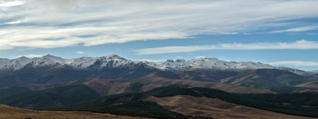 Scenic landscape of rugged mountains with patches of snow against a dramatic skyの写真素材
