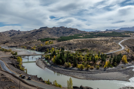 Andacollo aerial scenic view shows a river and a road winding through a landscape with mountains in the distance under a cloudy sky. Neuquen province, Argentinaの写真素材