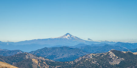 Prominent snowcapped Villarrica volcano rises above layers of hazy mountain ranges under a clear, blue sky in the distance. Patagonia, South Americaの写真素材
