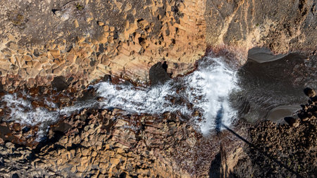 Aerial top view of Cabellera de la Virgen waterfall cascading over textured, rocky terrain into a dark pool. Caviahue, Neuquen, Argentinaの写真素材