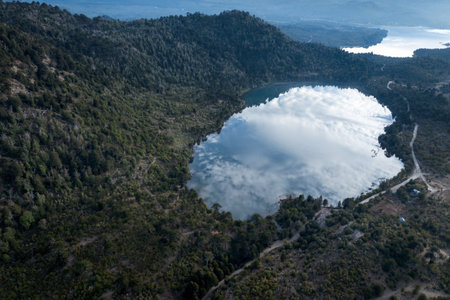 Aerial view of Laguna Verde reflecting the cloudy sky, surrounded by forested hills and mountains. ChaÃ±y Natural Reserve. Villa Pehuenia, Neuquen, Argentinaの写真素材