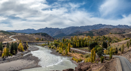 Scenic panoramic landscape showing mountains under a cloudy sky and river passing through valley in autumn sea. Andacollo, Neuquen, Argentinaの写真素材