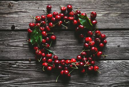 Frame, made of fresh picked cherries on rustic wooden background.