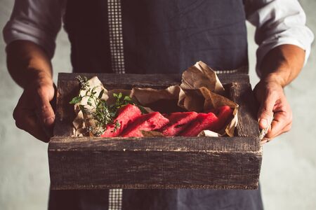 Male hands holding wooden bord with slieces of juicy ripe watermelon, that are stacked on top of each other, above the white table. Top-side view. Verticalの写真素材