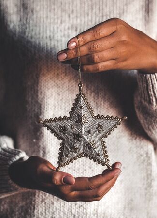 Woman in warm woolen sweater holding toy glass decorative star in hands, copy space, square crop. Christmas, new year holiday celebration conceptの写真素材