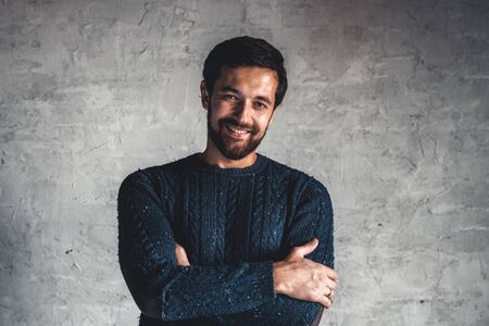 A man in a blue sweater on a gray background.