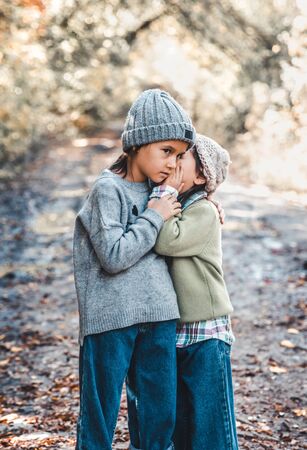 Little girl whispers a secret to her sistersitting against the background of nature. Sisters friendshipの写真素材