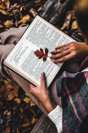 Autumn concept, an open book in the hands of a girl with yellow leaves