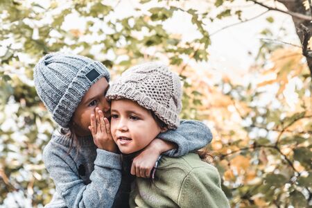 Little girl whispers a secret to her sistersitting against the background of nature. Sisters...