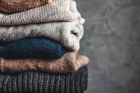 a stack of knitted warm cozy sweaters , on a chair by the gray wall. autumn, winter concept.