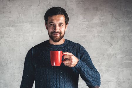 Dark-haired guy holds a red cup in his hand on a gray background