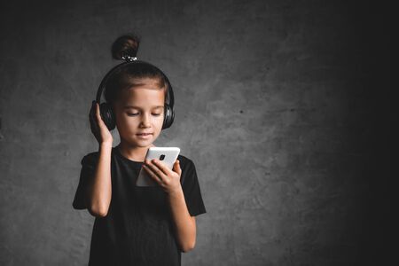 Little girl with headphones and phone on a gray backgroundの写真素材