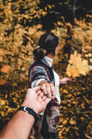 A young girl holds hands and leads a guy forward into the autumn to adventure, concept follow me
