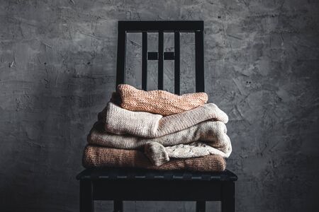a stack of knitted warm cozy sweaters , on a chair by the gray wall. autumn, winter concept.の写真素材