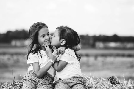 2 year old girl sitting on a bale of hay in the field at sunsetの写真素材