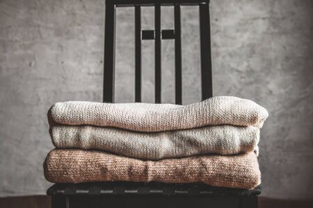 a stack of knitted warm cozy sweaters , on a chair by the gray wall. autumn, winter concept.の写真素材