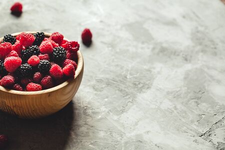 raspberries and blackberries in wood bowl on gray table, vintage