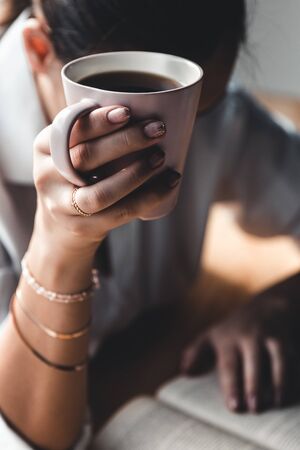 Beautiful woman in the morning drinks coffee and reads an old book in a white shirt. Education, drink.の写真素材