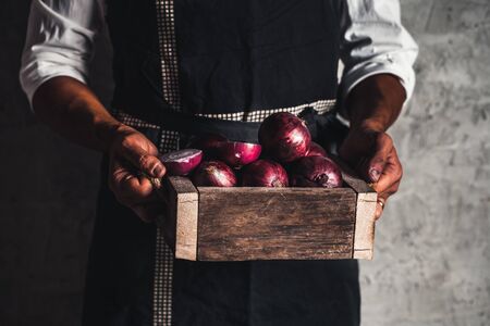 Fresh red onion in hands an old box. On wooden background.の写真素材