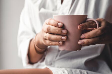 Woman in a white t-shirt holds morning coffee in a pink ceramic cup. Manicure. Front view