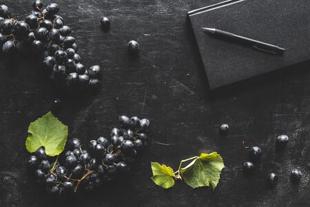 blue grapes on a dark background with a black notebook and a cup of coffee.の写真素材