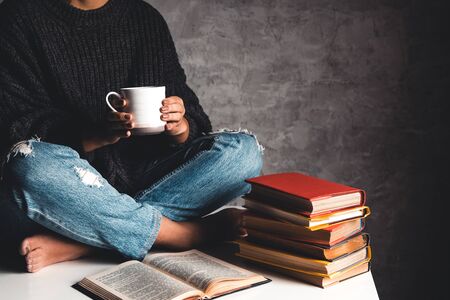 Girl reads books, study, develop with a cup of coffee on a white table and a gray background.の写真素材