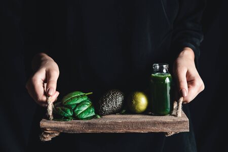 Girl holds a smoothie with spinach, avocado and lime on a vintage tray. Wholesome food, vegan, eco.
