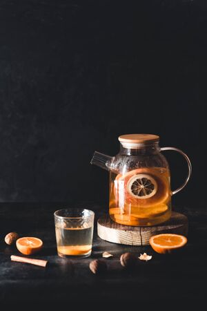 Citrus tea in a transparent teapot on a dark concrete background. Healthy drink, vegan, eco product.の写真素材