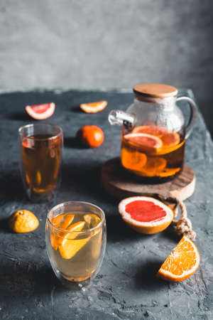 Citrus tea in a transparent teapot on a gray concrete background. Healthy drink, vegan, eco product.の写真素材