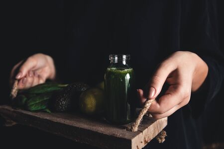 Girl holds a smoothie with spinach, avocado and lime on a vintage tray. Wholesome food, vegan, eco.