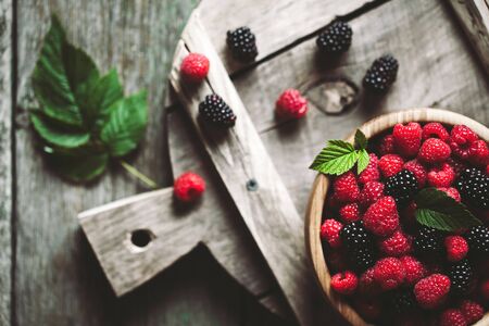 raspberries and blackberries on a wooden background in vintage style. Cutting board