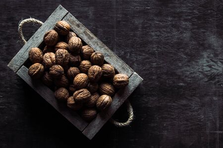 Box with tasty walnuts and nutcracker on dark wooden table, closeup