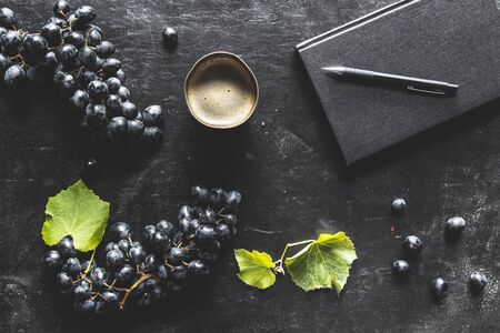 blue grapes on a dark background with a black notebook and a cup of coffee.の写真素材