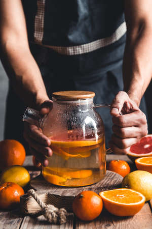 A man pours citrus tea on a wooden table. Healthy drink, vintage style. Vegan, eco products.の写真素材
