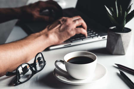 Business man using laptop computer and hand typing on laptop keyboard with notebook pen glasses and cup of hot coffeeの写真素材