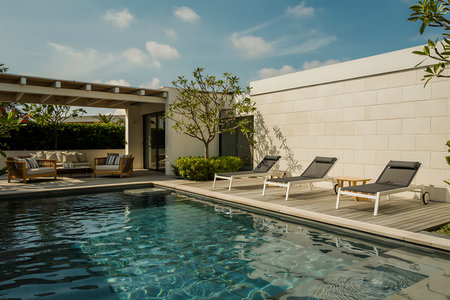 This luxurious villa boasts a stunning swimming pool and inviting lounge area perfect for a relaxing vacation retreat The contemporary design features sleek lounge chairs positioned on a wooden deck beside the crystal clear water An elegant pergola shades a comfortable seating area with plush cushions creating a tranquil oasis The modern architecture blends seamlessly with the natural surroundings under a bright summer sky The entire scene evokes a sense of serenity and upscale living making it the perfect escape for those seeking comfort and styleの素材