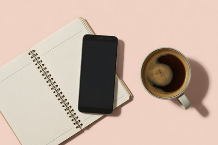 A minimalist flat lay featuring a cup of black coffee a smartphone and an open spiral notebook creating a clean and modern workspace aesthetic perfect for promoting productivity creativity and organization The neutral pink background provides ample copy space for adding text or graphics ideal for blog posts social media content or marketing materials conveying a sense of calm focus and professional efficiency This composition is suitable for diverse themes like remote work lifestyle blogging or business presentationsの素材